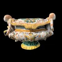 Saliera in maiolica con prese a forma di angeli che reggono dei libri e decoro a ‘raffaellesche