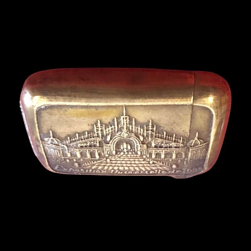 A small brass matchbox depicting the 1900 Paris World’s Fair.
