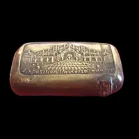 A small brass matchbox depicting the 1900 Paris World’s Fair.