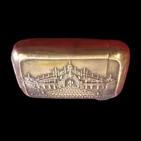 A small brass matchbox depicting the 1900 Paris World’s Fair.