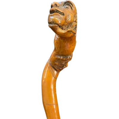 A traditional walking stick made of boxwood, featuring two grotesque figures and a snake.