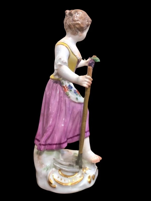 Sculturina in porcellana,figura di contadina con bastone e grappolo d’uva.Meissen.