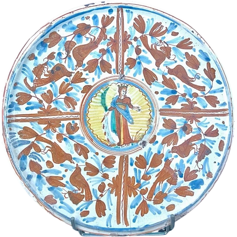 A majolica dish featuring calligraphic and naturalistic decorations, with a figure of a saint in the center