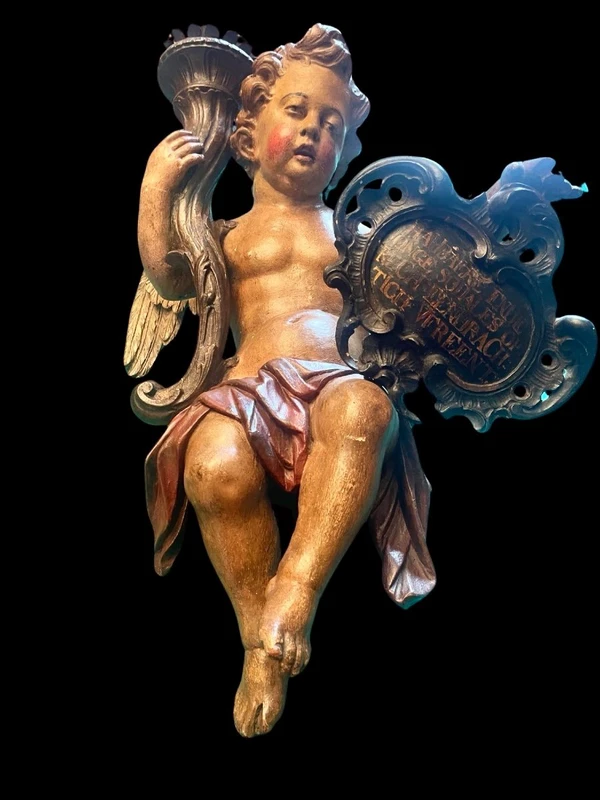 Polychrome wooden sculpture depicting an angel holding a candlestick and a rocaille shield