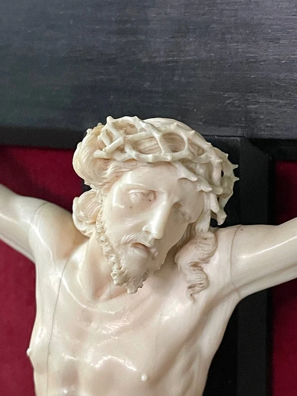 Cristo in avorio su croce in ebano e cornice sagomata in foglia oro.