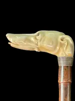 A cane with a side handle made of ivory in the shape of a greyhound's head.