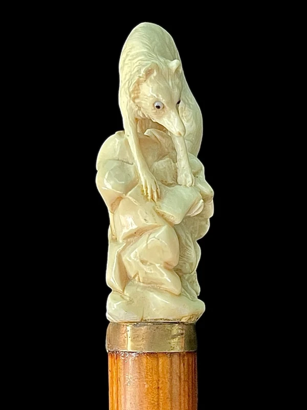 A walking stick with an ivory pommel depicting a wolf hunting prey hidden in a cave.