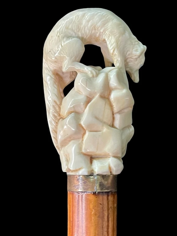 A walking stick with an ivory pommel depicting a wolf hunting prey hidden in a cave.