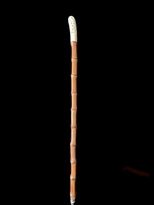 Cane with an ivory knob carved with figures and plant motifs; bamboo shaft.