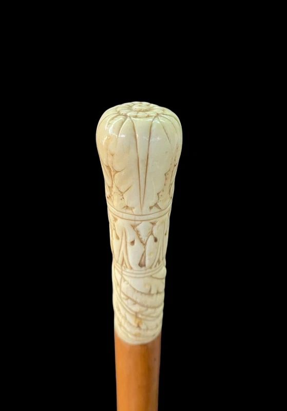 A walking stick with a spherical ivory pommel engraved with stylized plant motifs.