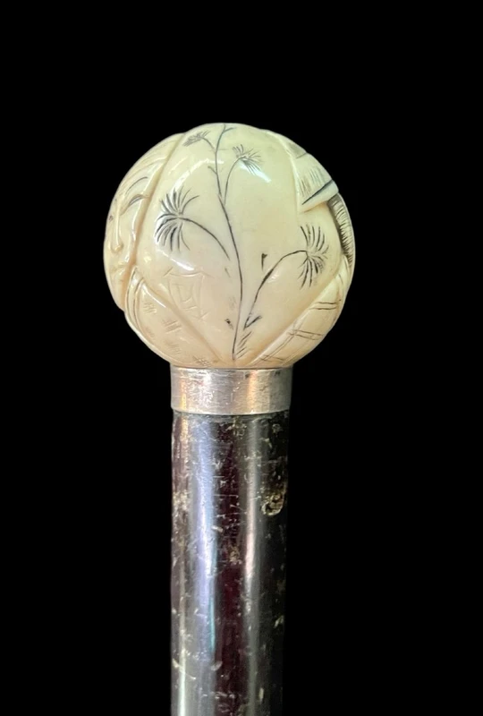A walking stick with a round ivory knob engraved with Japanese figures.