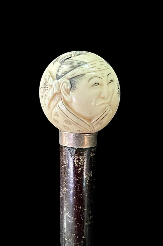 A walking stick with a round ivory knob engraved with Japanese figures.