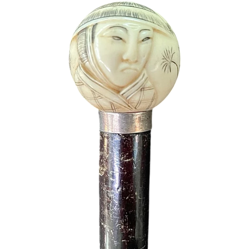 A walking stick with a round ivory knob engraved with Japanese figures.