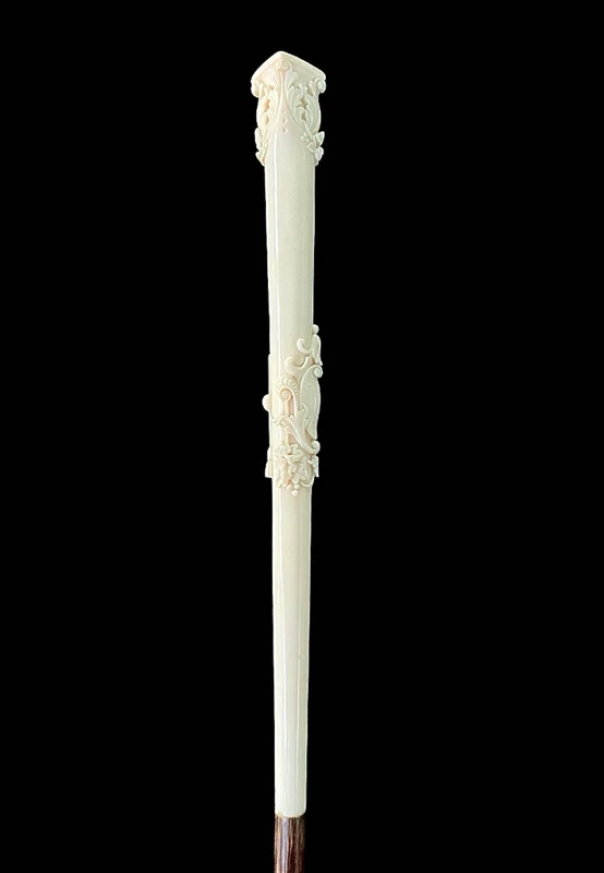 An evening cane with an ivory knob featuring a relief shield and rocaille motifs.