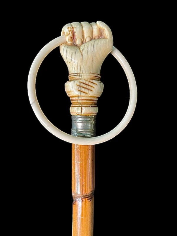 A walking stick with an ivory knob depicting a hand clutching a ring (glove holder).l