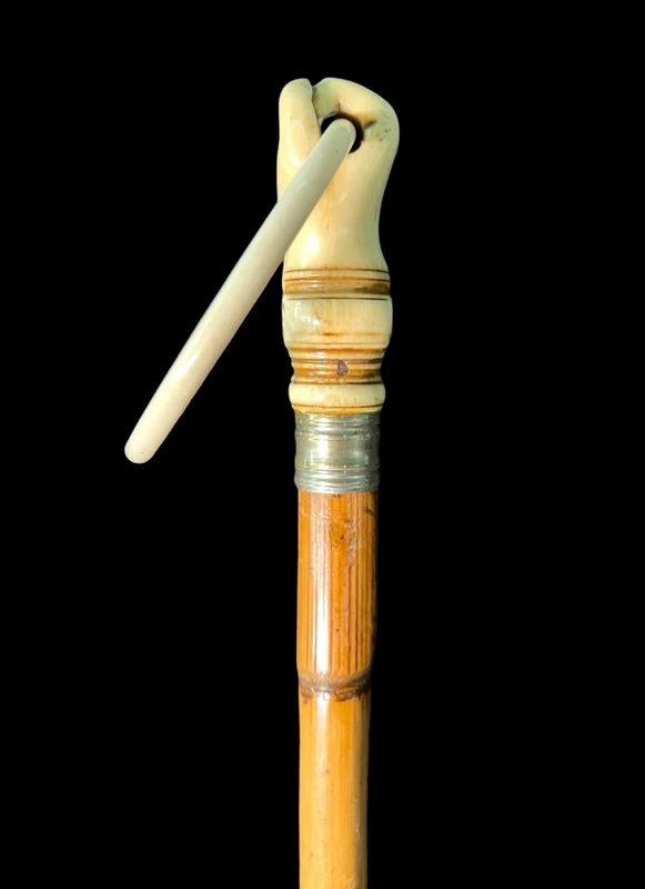 A walking stick with an ivory knob depicting a hand clutching a ring (glove holder).l