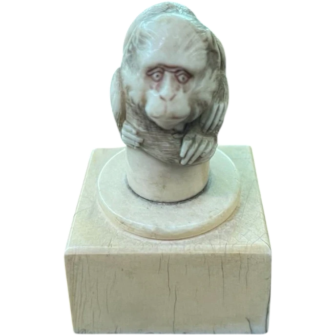 Petite sculpture en ivoire (poignée de canne) posée sur un socle carré et représentant un singe.