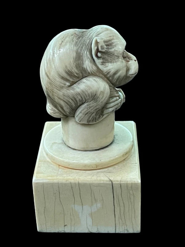 Petite sculpture en ivoire (poignée de canne) posée sur un socle carré et représentant un singe.