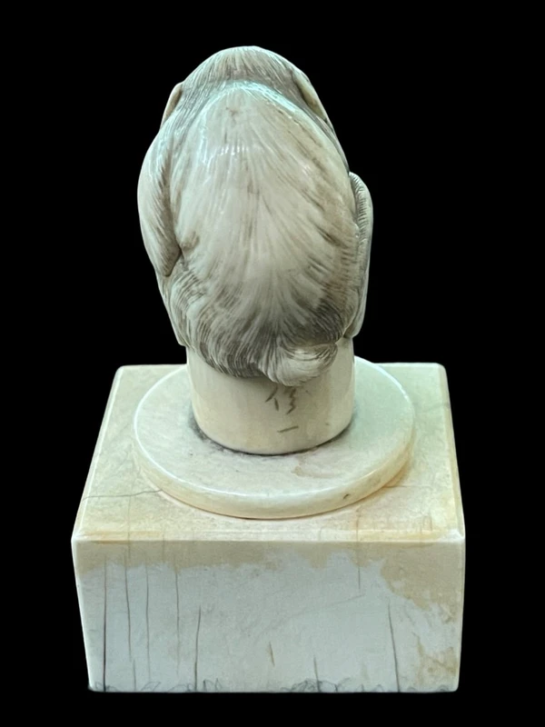 Petite sculpture en ivoire (poignée de canne) posée sur un socle carré et représentant un singe.