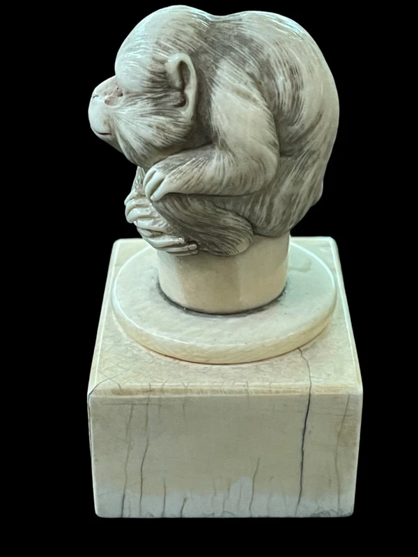 Petite sculpture en ivoire (poignée de canne) posée sur un socle carré et représentant un singe.