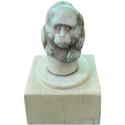 A small ivory sculpture (cane knob) on a square base depicting a monkey.