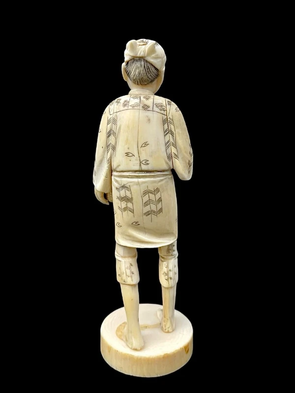 Sculpture okimono en ivoire représentant un personnage masculin portant un panier.