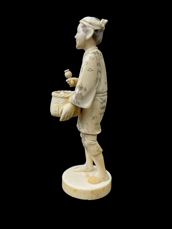 Sculpture okimono en ivoire représentant un personnage masculin portant un panier.