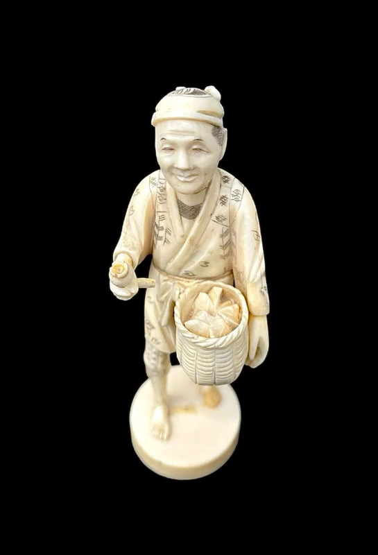 Sculpture okimono en ivoire représentant un personnage masculin portant un panier.