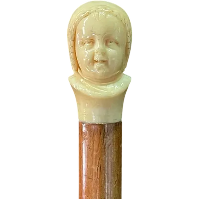 A walking stick with an ivory knob depicting the dual face of a child—one laughing, the other crying.