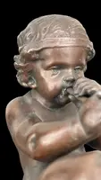 A small bronze sculpture depicting a cherub playing the flute.