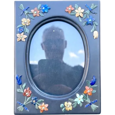 A slate frame with floral motifs created using a micro-mosaic of relief-carved semi-precious stones.