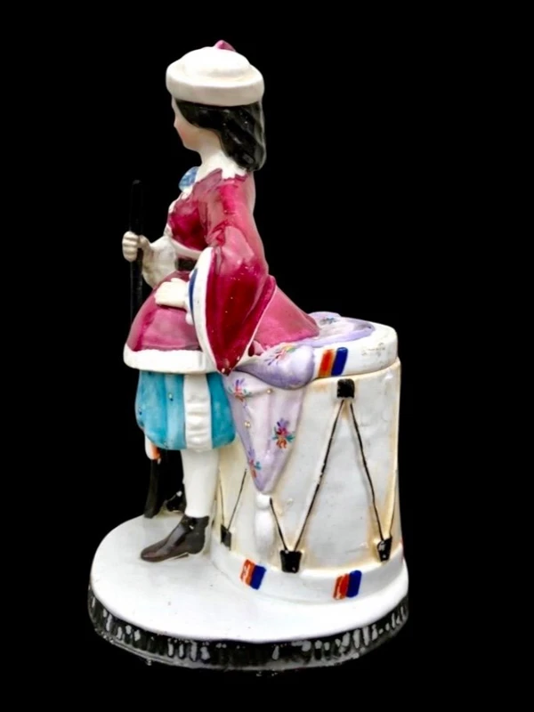 Porcelain tobacco box featuring a female figure with a rifle and a drum.