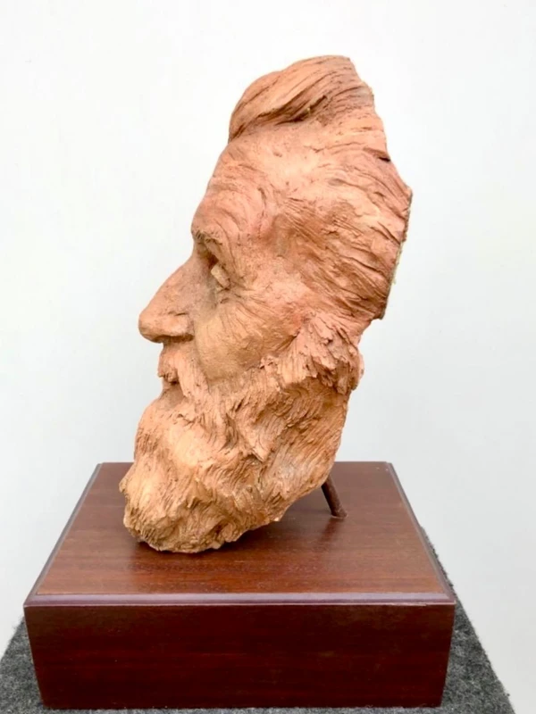 Terracotta sculpture depicting the head of a bearded man. Wooden base.