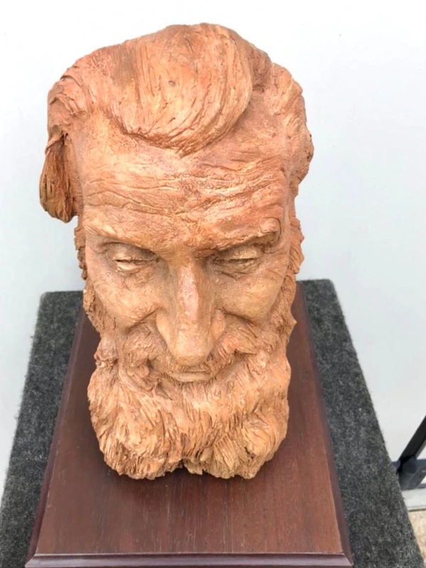 Terracotta sculpture depicting the head of a bearded man. Wooden base.