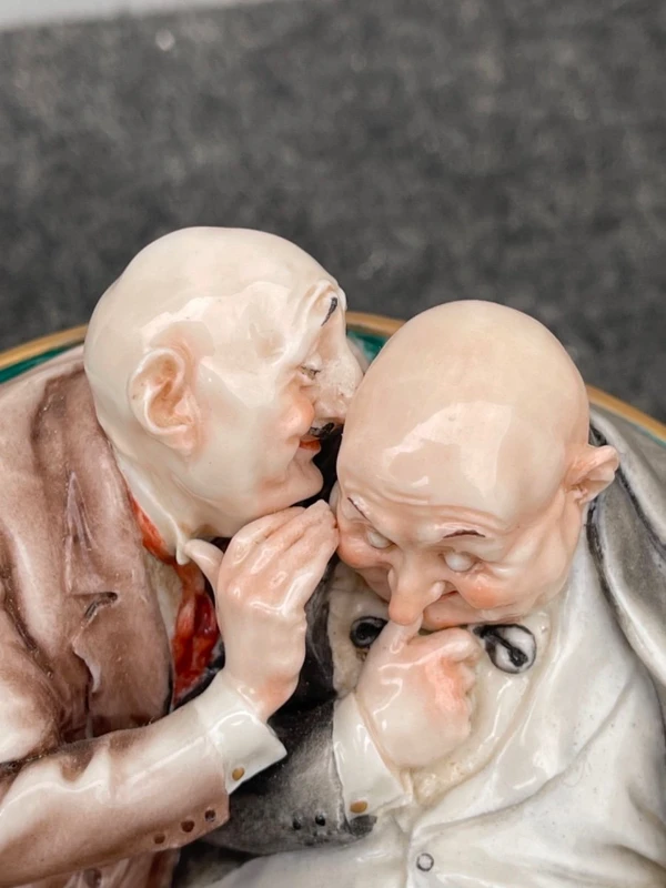 Sculpture caricaturale en porcelaine représentant deux amis qui se chuchotent à l'oreille.