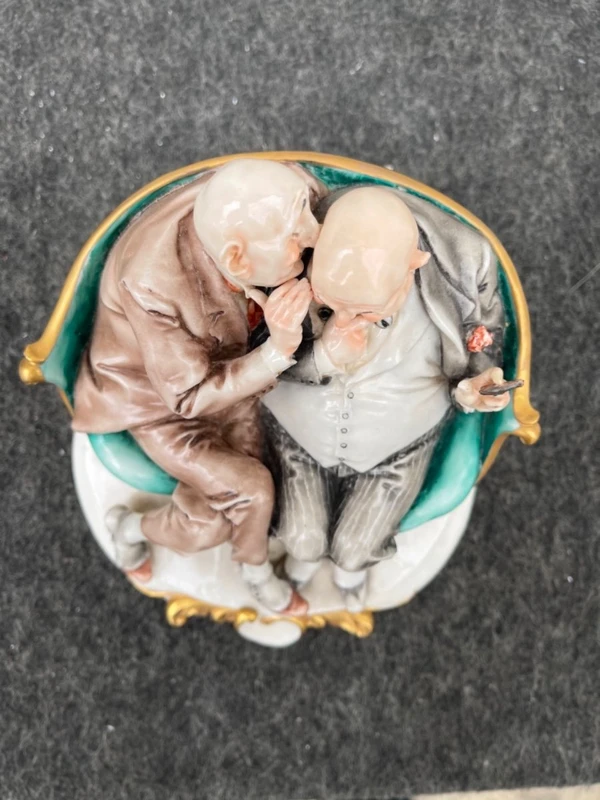 Sculpture caricaturale en porcelaine représentant deux amis qui se chuchotent à l'oreille.