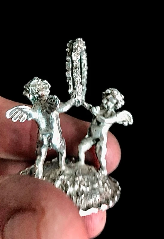 Serie di sei segnaposti in argento con coppia di putti che reggono una ghirlanda.
