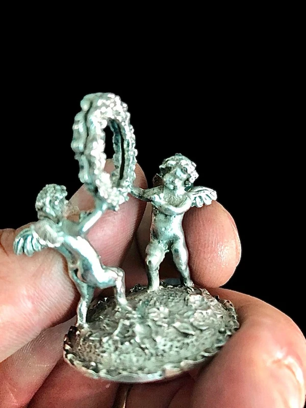 Serie di sei segnaposti in argento con coppia di putti che reggono una ghirlanda.
