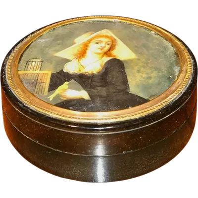A small papier-mâché box with a miniature figure depicting a lady with a little bird.