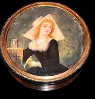 A small papier-mâché box with a miniature figure depicting a lady with a little bird.