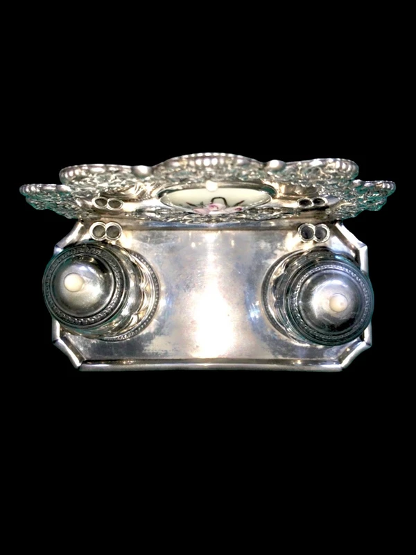 An inkwell made of embossed and openwork silver with stylized plant motifs and an enamel medallion.