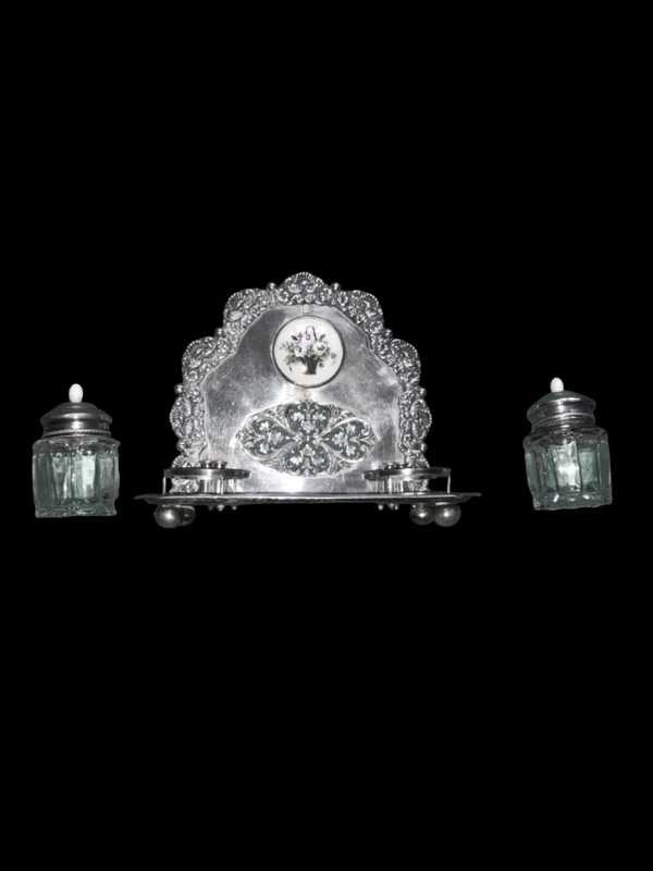 An inkwell made of embossed and openwork silver with stylized plant motifs and an enamel medallion.