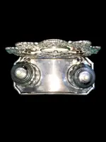An inkwell made of embossed and openwork silver with stylized plant motifs and an enamel medallion.