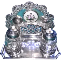 An inkwell made of embossed and openwork silver with stylized plant motifs and an enamel medallion.