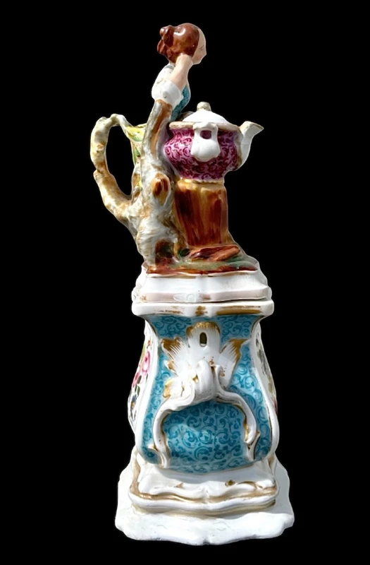 Decorated porcelain teapot-shaped nightlight with a lid shaped like a seated lady holding a teapot.
