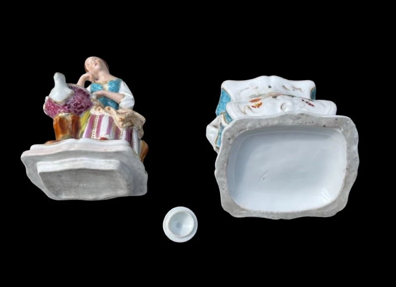 Decorated porcelain teapot-shaped nightlight with a lid shaped like a seated lady holding a teapot.