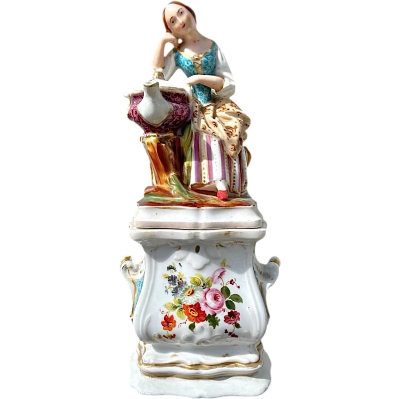 Decorated porcelain teapot-shaped nightlight with a lid shaped like a seated lady holding a teapot.