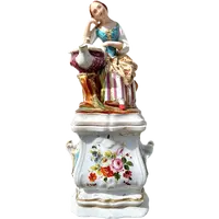 Decorated porcelain teapot-shaped nightlight with a lid shaped like a seated lady holding a teapot.