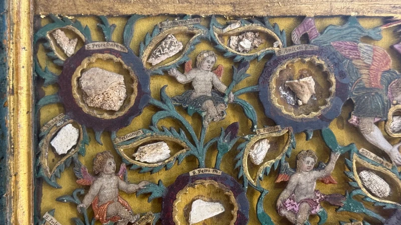 Quadro reliquiario con composizione in legno traforato in rilievo con putti e motivi vegetali.