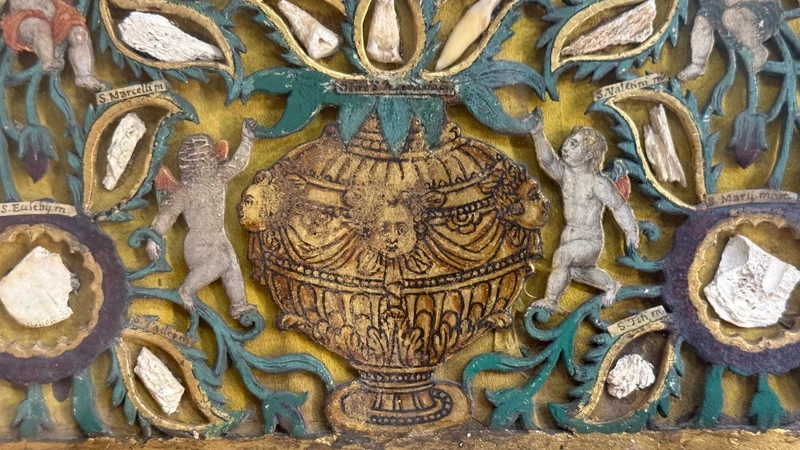 Quadro reliquiario con composizione in legno traforato in rilievo con putti e motivi vegetali.